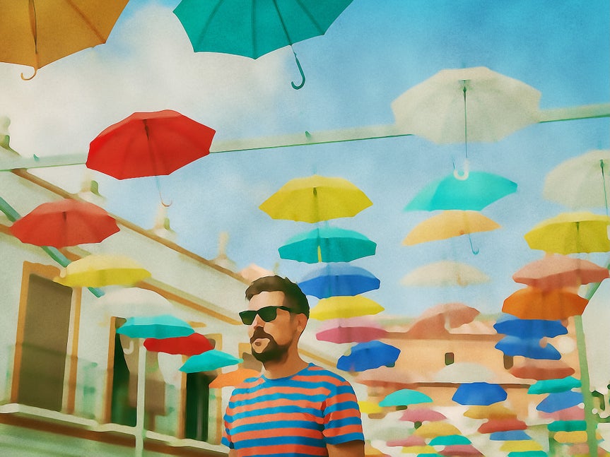 The same scene of a man under hanging umbrellas, enhanced with a soft watercolor photo filter that adds vibrant colors and a painterly effect.